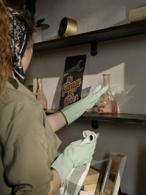 Hands in yellow gloves cleaning wall with sponge and spray bottle.